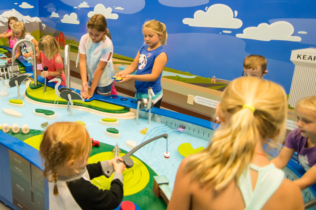 Children playing at interactive indoor water and play fishing exhibit.
