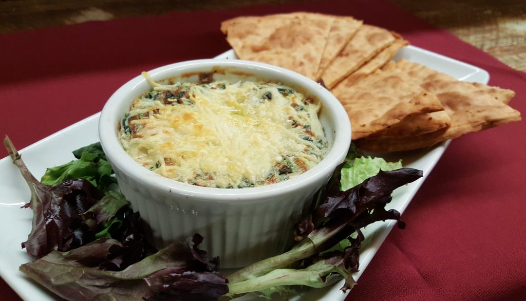 artichoke dip topped with cheese and side of chips