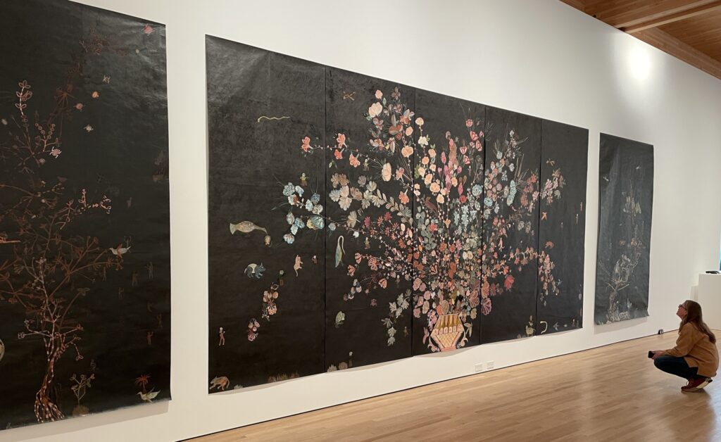 painting of vase overflowing with flowers on a black canvas sheet.