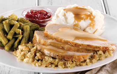 Thanksgiving plate of sliced turkey, stuffing, green beans, cranberry sauce, and creamy mashed potatoes with gravy. 