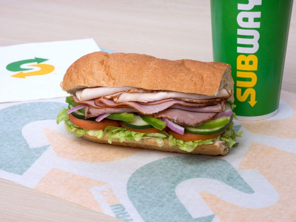 Subway turkey, ham, and roast beef toasted sandwich with a subway drink cup. 