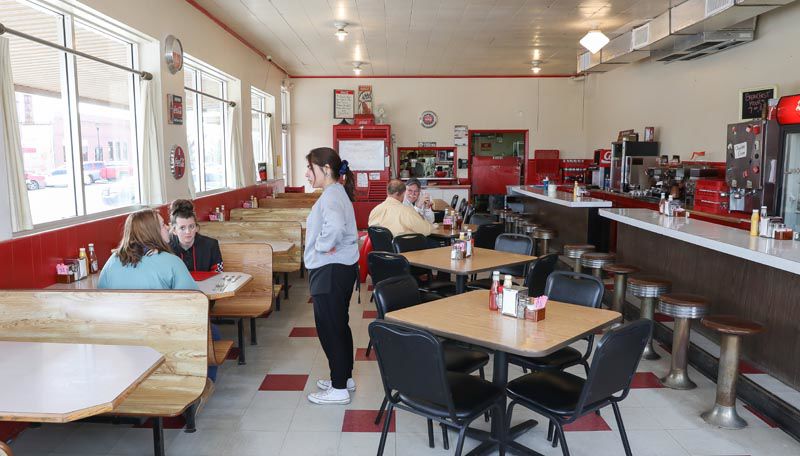 Server taking order from customer. Cafe has a diner theme with red, black, and white colors. 