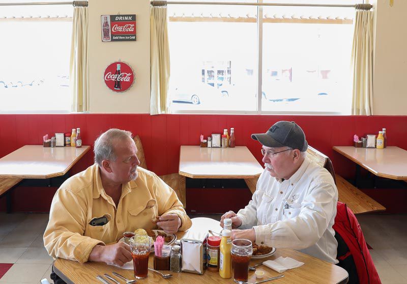 Two older gentleman eating breakfast and talking. 