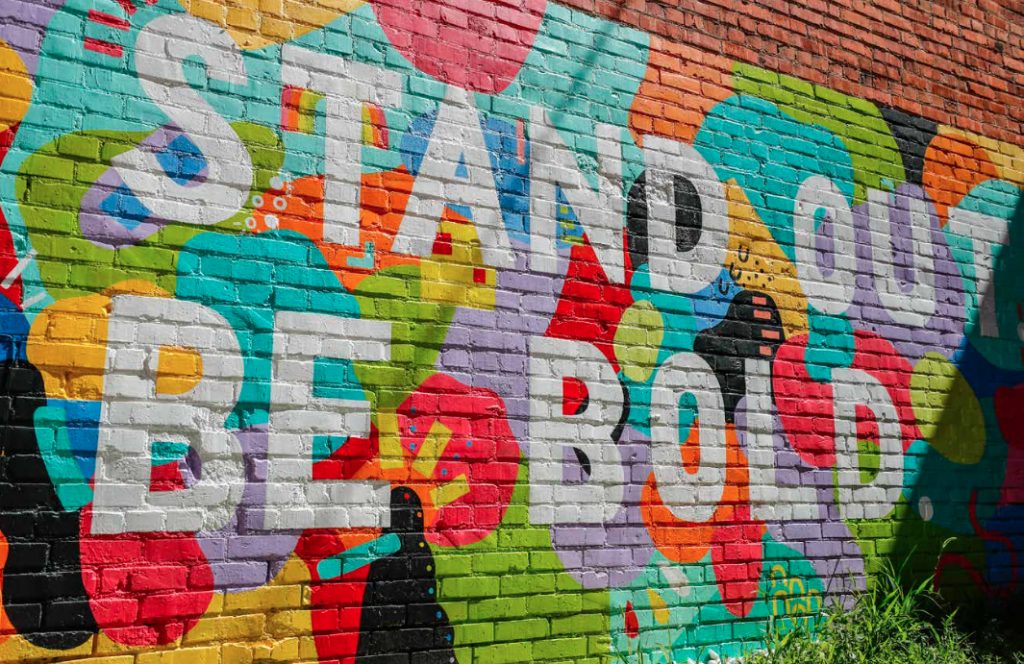 Colorful brick wall mural with words stand out be bold painted =. 
