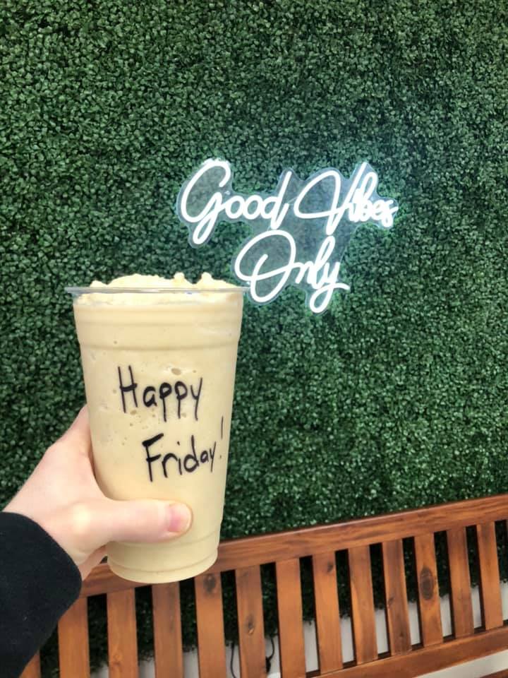 Person holding shake with Happy Friday written on it with greenery background and Good Vibes Only light up sign. 
