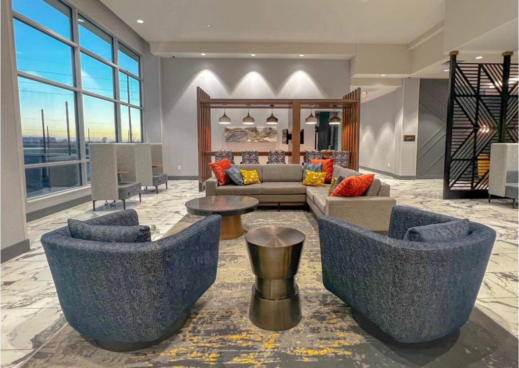 sectional yellow and grey rug under blue chairs and grey sectional couch, and wall of windows in lobby