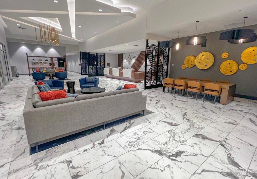 modern hotel lounge, grey sectional couch, marble flooring, and rectangle table with wood chairs