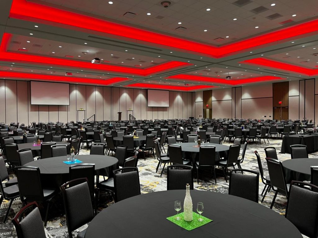 empty circular table and chairs in conference hall, grey patterned carpet and red lights lining ceiling.