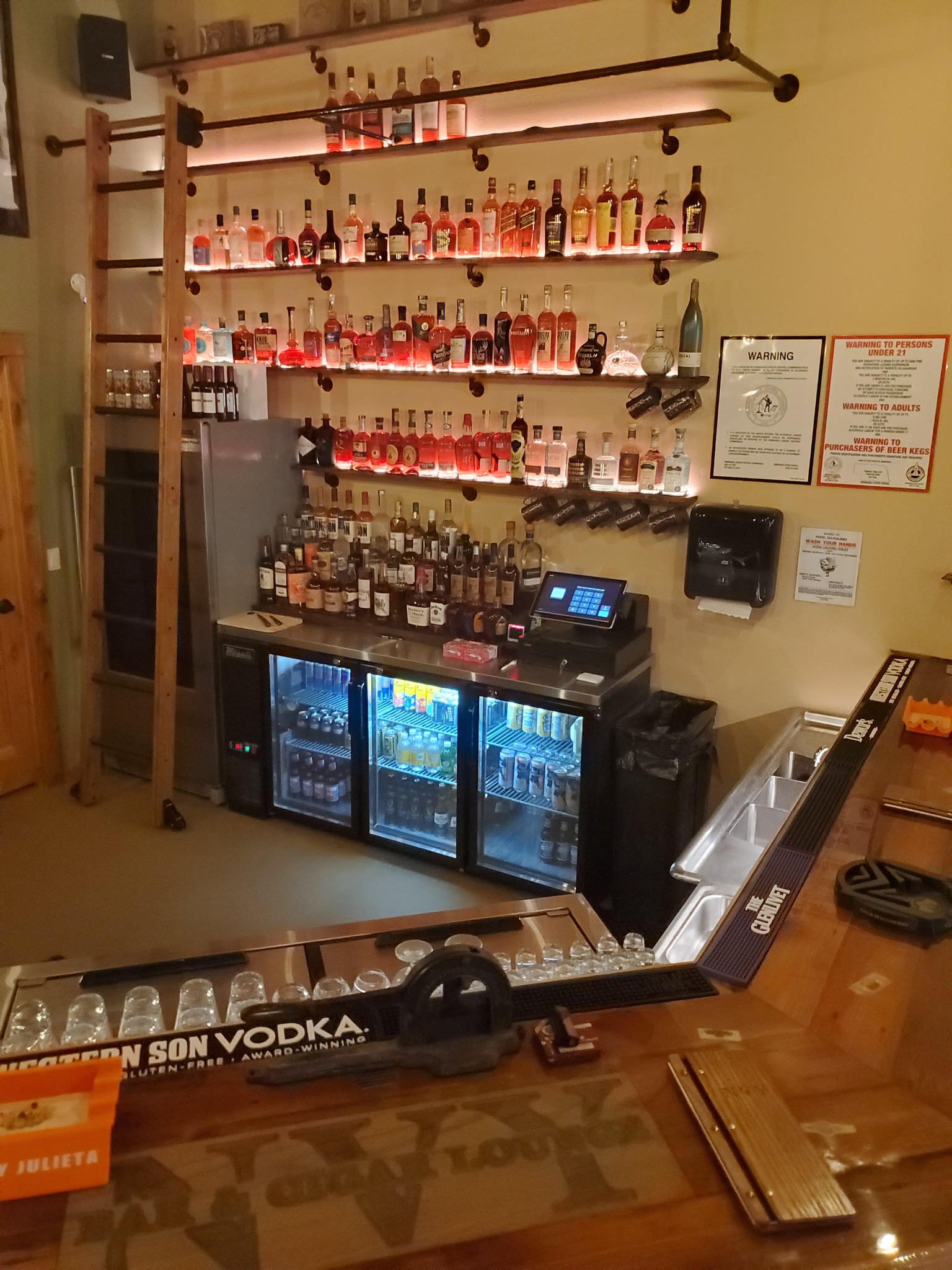 bar area and wall lined with shelves holding hard liquor. 