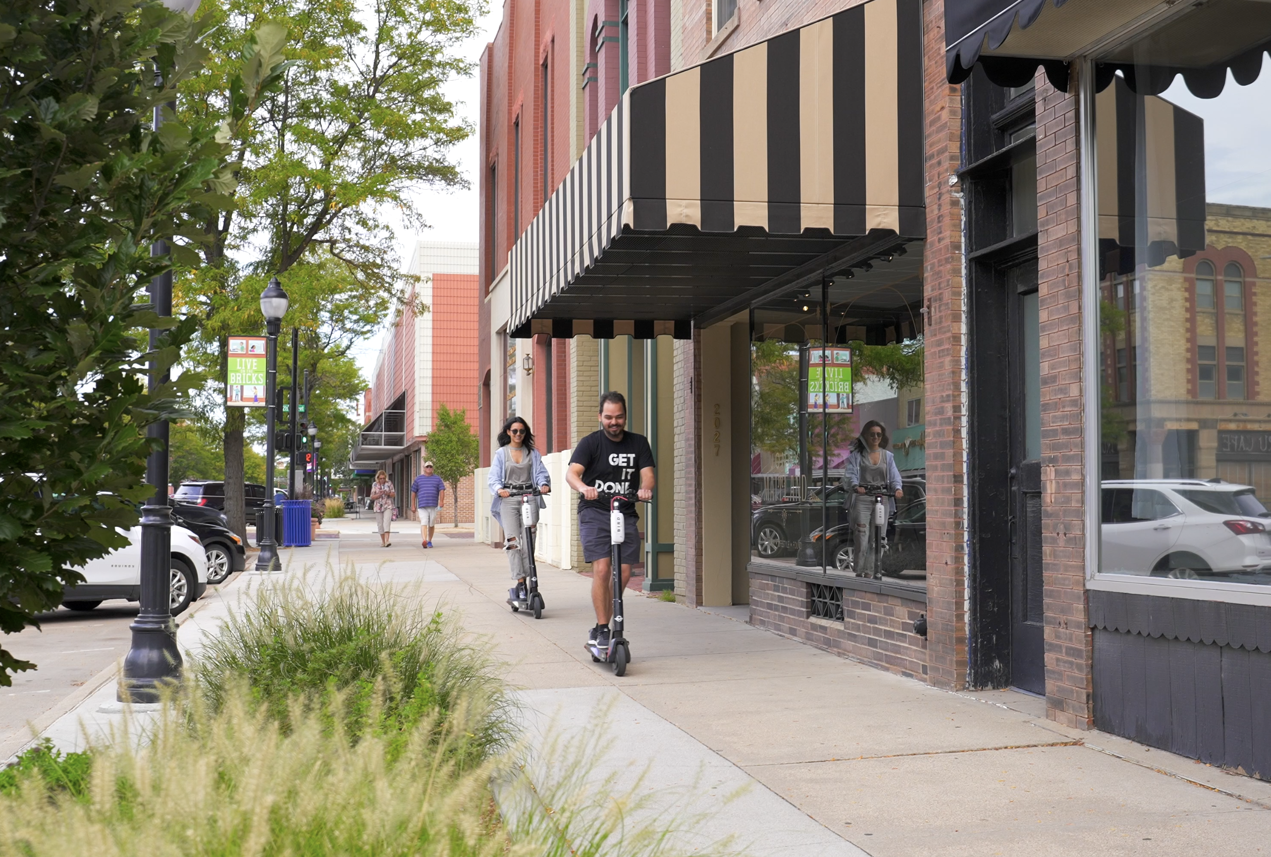 People riding on scooters on the sidewalk in downtown.