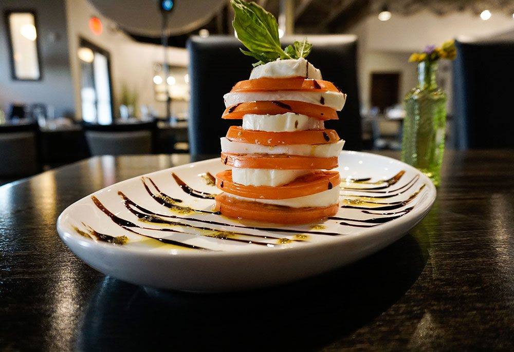 stack of tomatoes and mozzarella slices topped with a basil leaf and balsamic drizzle.