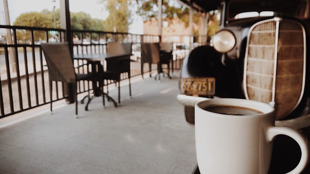 Mug of coffee sitting on table in patio next to vintage car .