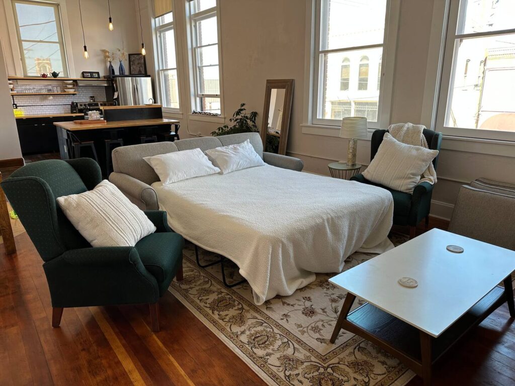 pull out couch with white blankets and pillows. Tall windows outlooking downtown Kearney. 