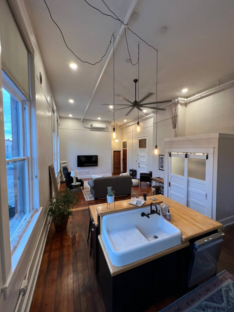kitchen area, wood island with counter space and sink. hanging lights and large fan on ceiling. 
