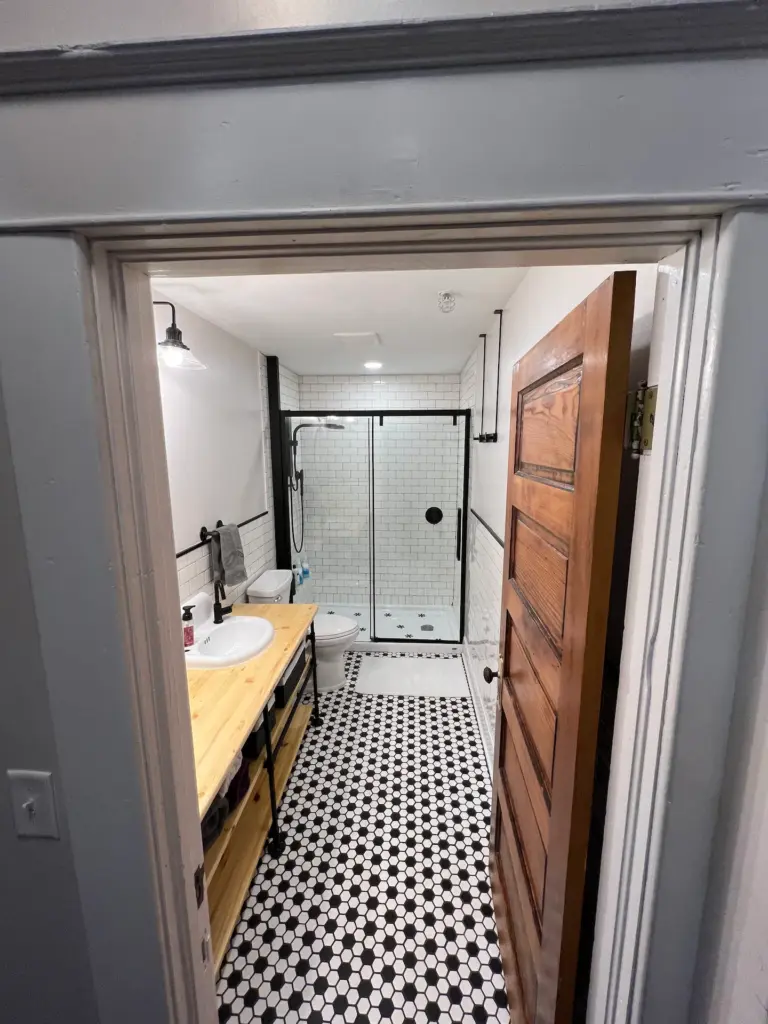 black and white tiled bathroom with walk in shower. Long wooden counter with sink and towels. 