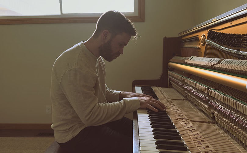 Man playing the piano as light streaming in through the window.