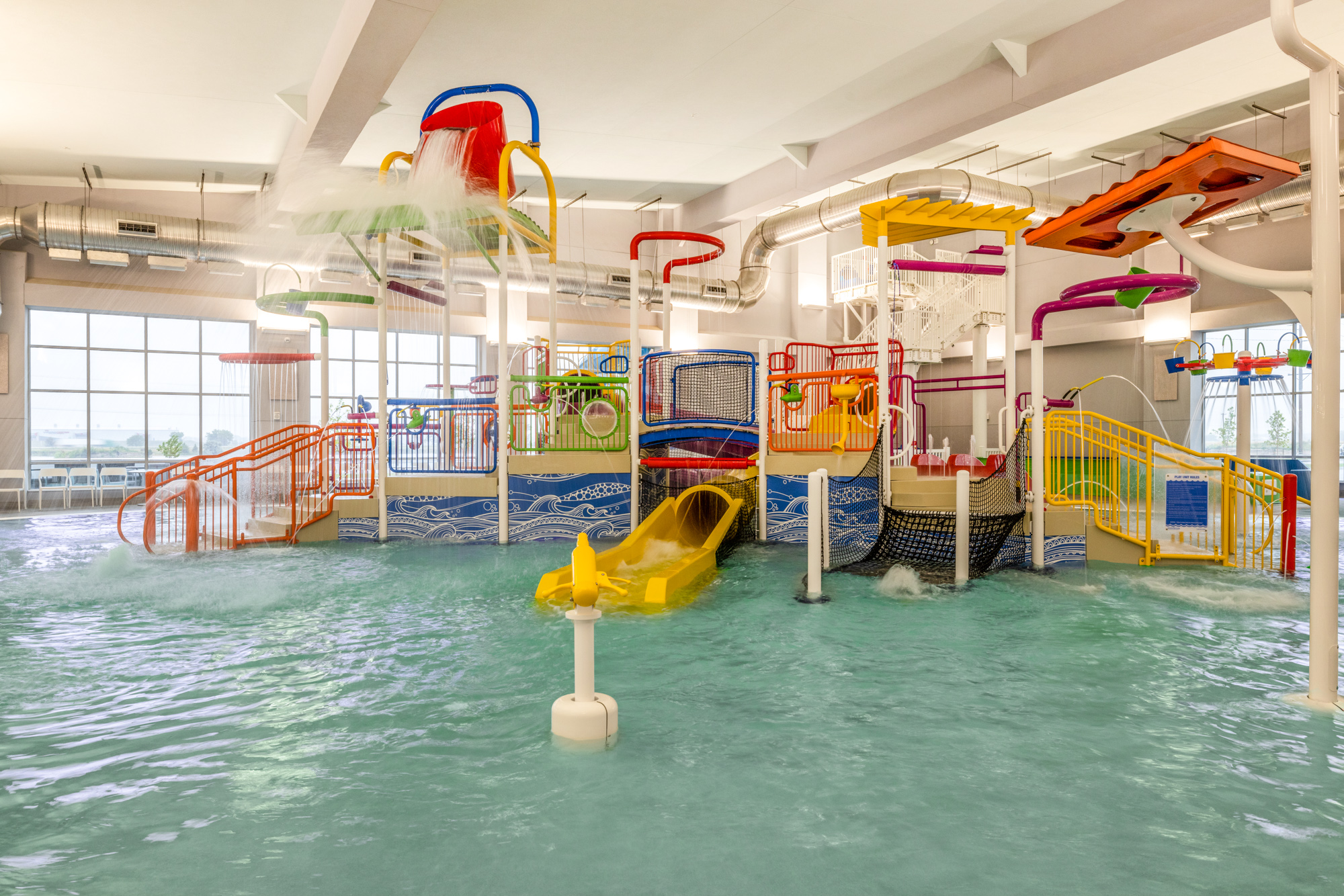 Wide indoor swimming pool area with a waterslide structure to one side, and a smooth concrete deck surrounding the water.