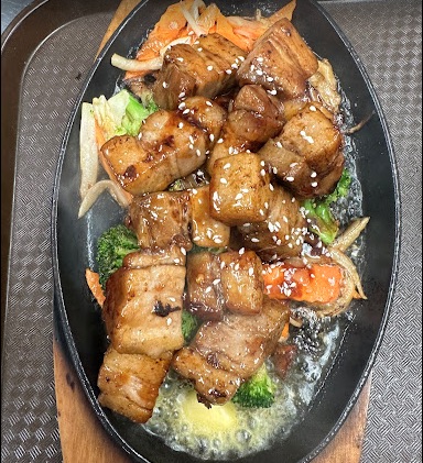stir fry of chicken and broccoli, bubbling with sauce in a oval skillet. 