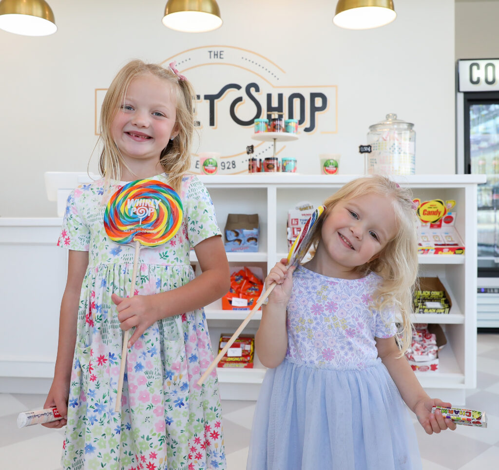 Two children smiling as they hold giant lollypops inside the Sweet Shop. 