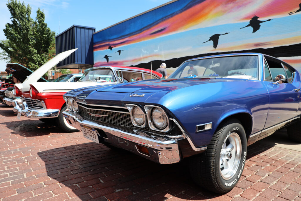 Classic Cars parked outside on display in-front of sandhill crane mural. 