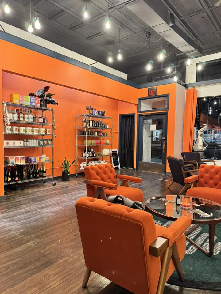 interior of shop with orange walls and shelves displaying cans and bottles. Orange cushion chairs seated around a glass table. 