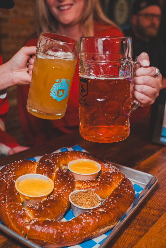 clinking of beer glasses over large salted pretzel 