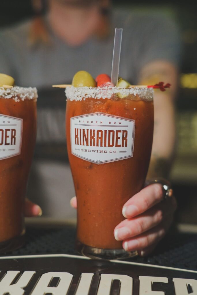 Bartender serving Bloody Mary with salt rim and olive skewer. 